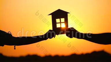 一男一女抱着纸屋对着夕阳.. 屋的剪影.. 建筑主题，真实